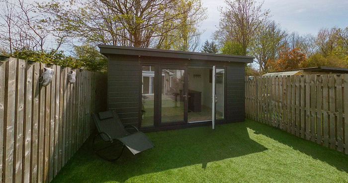 A modern timber-clad garden room with glazed doors in a landscaped back garden.